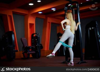 a young Caucasian woman in a white sports uniform does leg exercises with an expander . not a professional athlete, a beginner.. a young Caucasian woman in a white sports uniform does leg exercises with an expander . not a professional athlete, a beginner