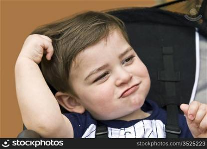 A young child in a stroller making a funny face with hand in hair.