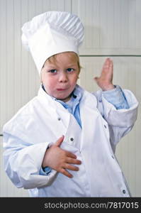 A young child wearing a chef&rsquo;s uniform and toque, liking what he tastes