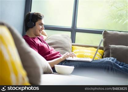 A YOUNG COLLEGE STUDENT ATTENDING ONLINE CLASS WHILE RESTING ON SOFA