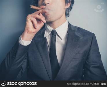 A young confident businessman is smoking a cigar