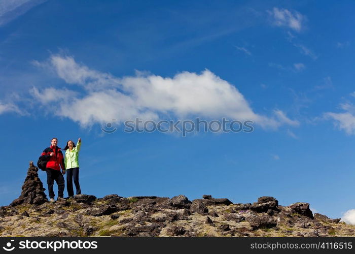 A young couple hiking in stony mountains standing next to a stone pile tor or signpost pointing to the distance. Shot on location in Iceland.