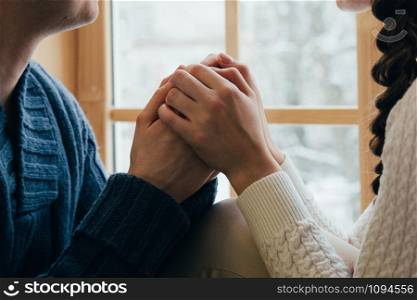 A young couple holding their hands together by the window