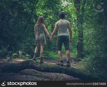 A young couple is holding hands and are standing on a log in the forest