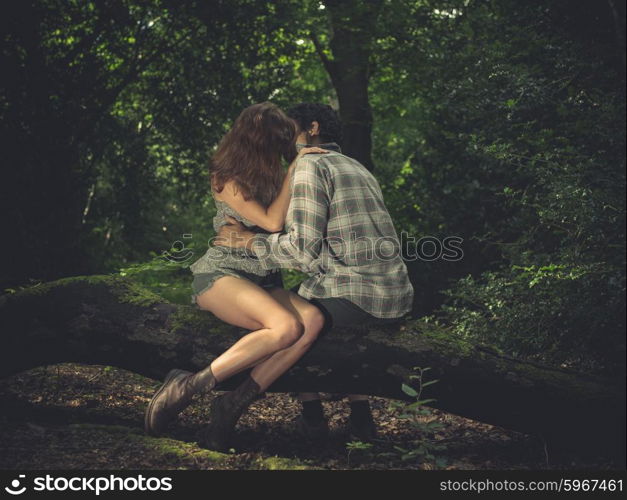 A young couple is sitting on a log in the forest and kissing