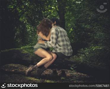 A young couple is sitting on a log in the forest and kissing