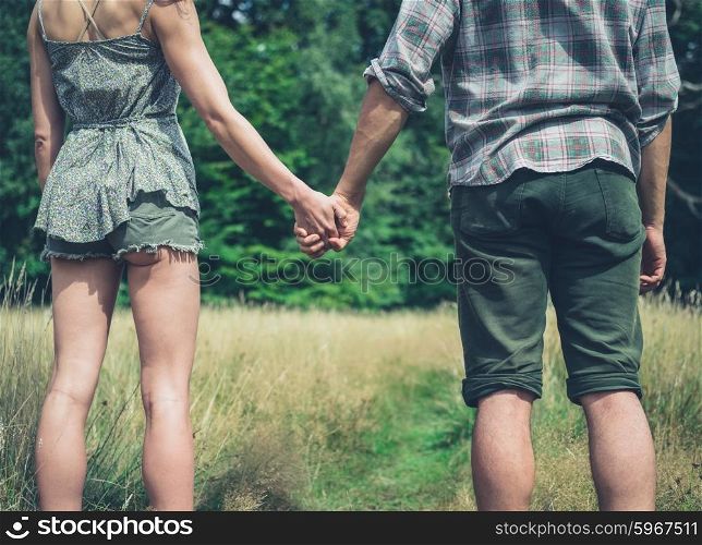 A young couple is standing in a meadow in the forest and holding hands