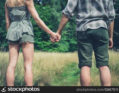 A young couple is standing in a meadow in the forest and holding hands