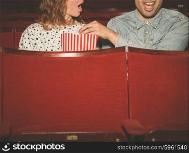 A young couple is watching a film in a movie theater and the man is stealing the woman&rsquo;s popcorn to her dismay