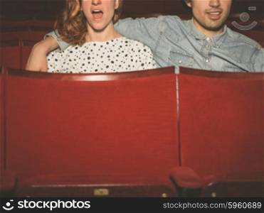 A young couple is watching an exciting film in a movie theater
