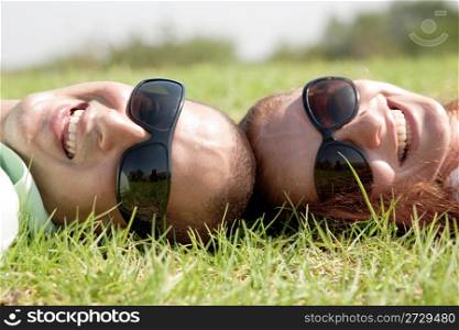 A young couple laying down and smiling on a grass lawn