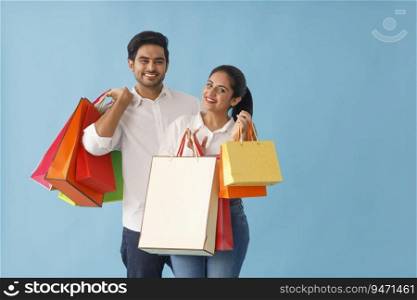 A YOUNG COUPLE PLAYFULLY POSING WITH SHOPPING BAGS IN HAND