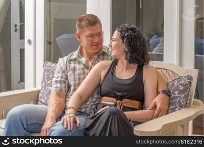 A young couple sit together on the porch of their home.