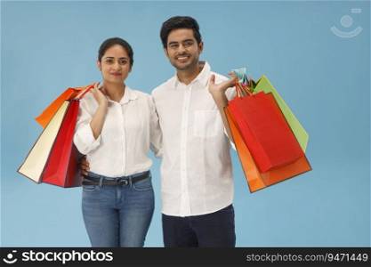 A YOUNG COUPLE STANDING IN FRONT OF CAMERA HOLDING SHOPPING BAGS
