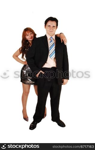 A young couple standing in the studio, he in a black suit and she in an silverevening dress and bright read hair for white background.