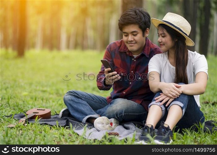 A young couple using and looking at mobile phone while sitting in the park together