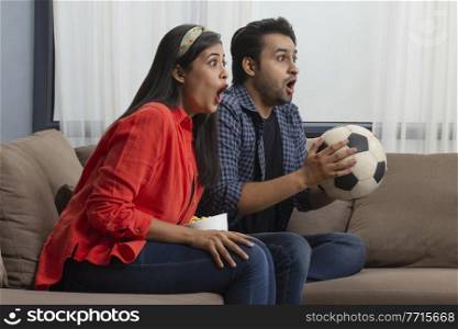 A young couple watching a football match excitedly in a room.