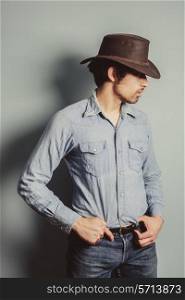 A young cowboy is standing by a blue wall