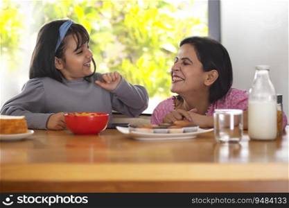 A YOUNG DAUGHTER AND MOTHER PLAYFULLY SITTING WITH EACH OTHER WHILE EATING FOOD