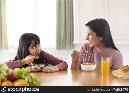 A YOUNG DAUGHTER LOOKING AT MOTHER WHILE HAPPILY EATING BREAKFAST