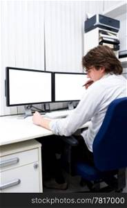 A young designer chewing his pen in thoughts, sitting behind a computer work station.