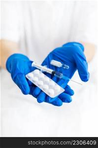 A young doctor holds a vaccine, syringe and pills in latex blue gloves. Doctor indoors makes vaccination. A woman in a medical office. Vaccination against influenza and viruses. A young doctor holds a vaccine, syringe and pills in latex blue gloves. Doctor indoors makes vaccination. A woman in a medical office. Vaccination against influenza and viruses.