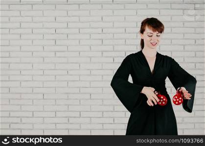 a young elegant woman in black dress, dancing flamenco with red castanets, smiling, white brick wall in the background