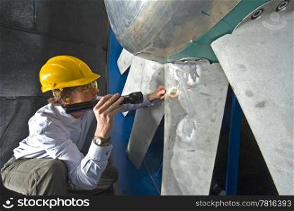 A young engineer inspecting the blades of an industrial windtunnel wearing a hard top, earplugs and protective goggles