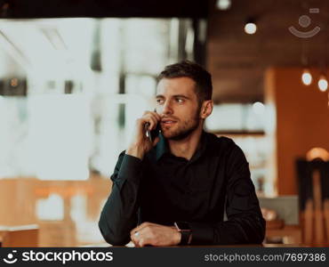 a young entrepreneur sits in a cafe and uses smartphone during a coffee break. a young businessman in a black shirt sits in a coffee shop and uses smartphone during a coffee break.