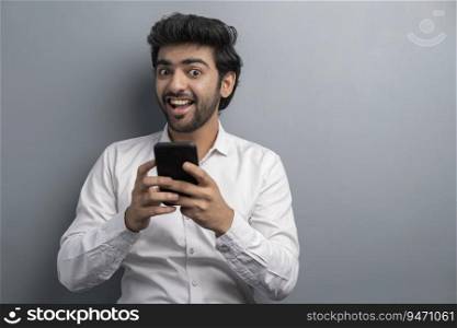 A YOUNG EXECUTIVE HAPPILY LOOKING AT CAMERA WHILE USING MOBILE PHONE