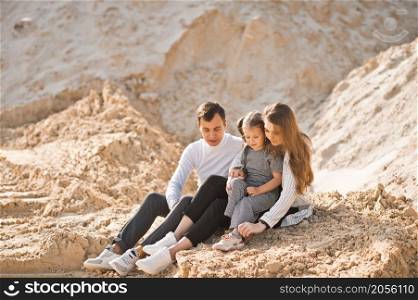 A young family is sitting among the sandy mountains.. A family of three is sitting among mountains of sand 3350.