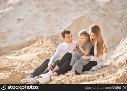 A young family is sitting among the sandy mountains.. A family of three is sitting among mountains of sand 3352.