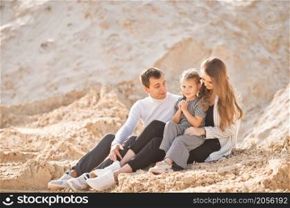 A young family is sitting among the sandy mountains.. A family of three is sitting among mountains of sand 3353.