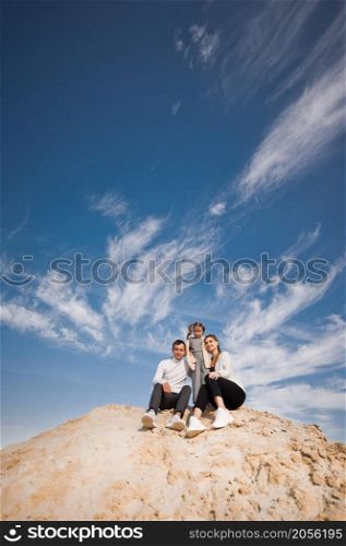A young family with a daughter among the sand and blue sky.. A family poses standing on a mountain of sand against the sky 3312.