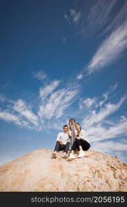 A young family with a daughter among the sand and blue sky.. A family poses standing on a mountain of sand against the sky 3312.
