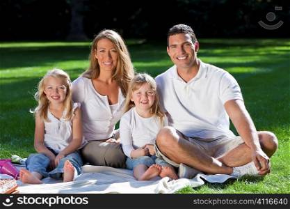 A young family with mother father and two blond daughters having a picnic in a sun bathed green park