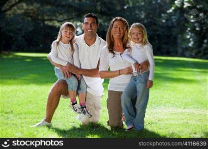 A young family with mother father and two blond daughters having fun in a sun bathed green park