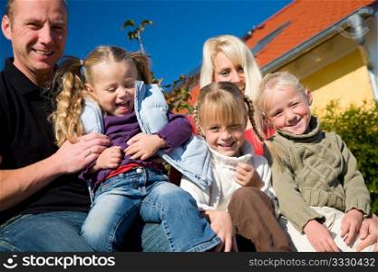 A young family with three children in front of their new home sitting in the sun