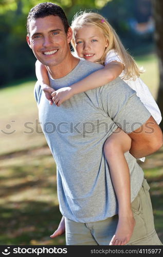 A young father with his blond daughter on his shoulders having fun in a sun bathed green park