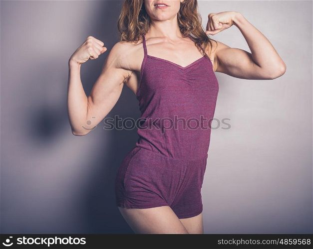 A young female bodybuilder is posing and showing of the muscle definition in her arms