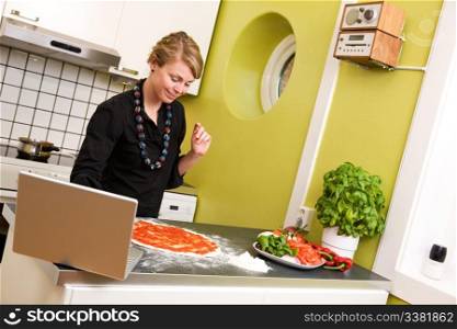 A young female cooking the the kitchen following a recipe on the computer.