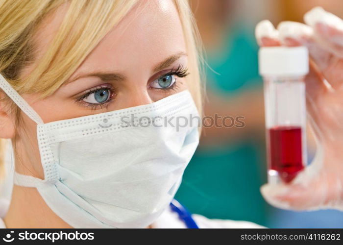 A young female doctor/nurse looking at a blood sample with other medical staff out of focus in the background