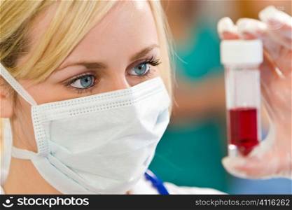 A young female doctor/nurse looking at a blood sample with other medical staff out of focus in the background