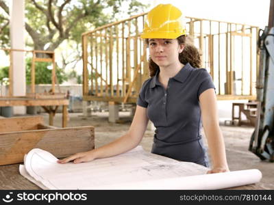 A young female engineering student examining blueprints on a construction site.