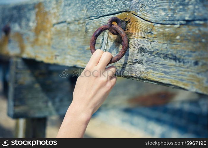 A young female hand is grabbing an old rusty chain attached to a wooden beam