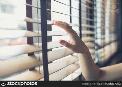A young female hand is touching some venetian blinds by the window