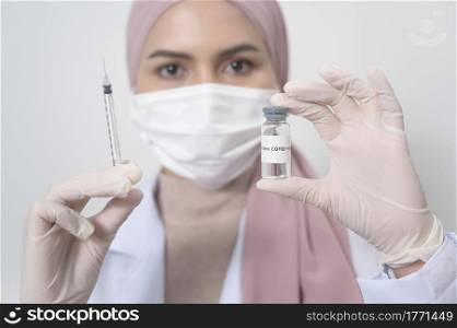 A young female muslim doctor holding a syringe with covid-19 vaccine bottle for injection, covid-19 vaccination and health care concept. Young female muslim doctor holding a syringe with covid-19 vaccine bottle for injection, covid-19 vaccination and health care concept