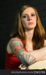 A young female with serious stare and arm tattoo.