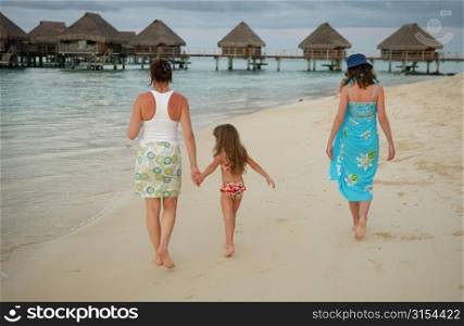 A young girl (6-8) walking with two young women on a beach, Moorea, Tahiti, French Polynesia, South Pacific