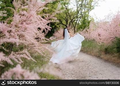 a young girl bride in a white dress is spinning on a path in a spring forest on a wedding day
